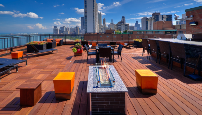 The roof deck of 1350 North Lake Shore apartments on a clear, sunny day. The city of Chicago skyline is the background and an inviting fire pit offers warmth to the seats around it in the foreground.