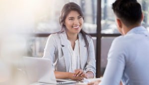 A smiling woman speaks with a client at her desk.