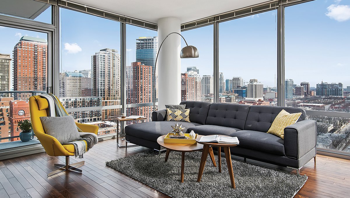 The corner of a living room at Burnham Pointe with a couch and chair sitting around a coffee table. The floor-to-ceiling windows line the room where the city skyline is viewed.