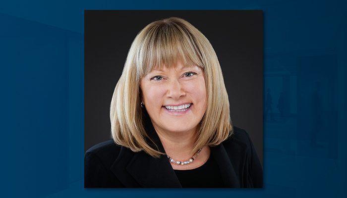 Professional portrait of Julie F. Stevlingson, a woman with shoulder-length blonde hair and bangs, wearing a black blazer and a pearl necklace, smiling against a dark background.