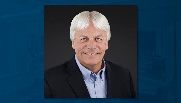 Professional portrait of Todd Bancroft, a man with white hair wearing a black blazer and light blue shirt, smiling against a dark background.