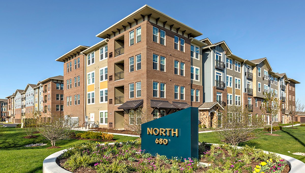 An exterior view of North 680 apartments. The blue North 680 sign is in the foreground, surrounded by a flowerbed. The building itself is in the background.
