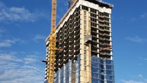 An exterior photograph of the Aspire Residences tower under construction. A crane works on the left of the building. Window glass is installed roughly half way up the building.