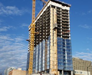 An exterior photograph of the Aspire Residences tower under construction. A crane works on the left of the building. Window glass is installed roughly half way up the building.