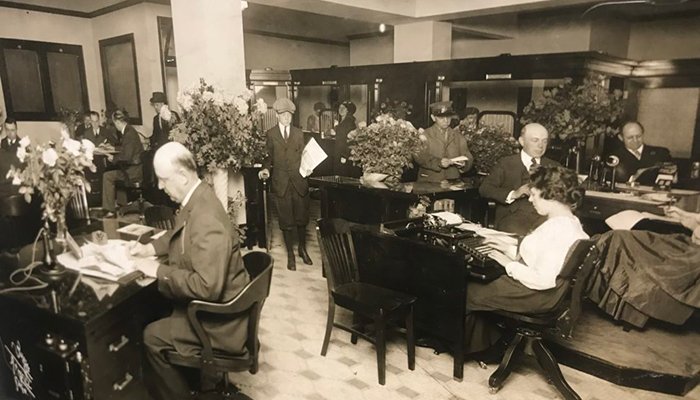 One of the first Draper and Kramer offices with several people in period clothing sitting at desks and reviewing paperwork.