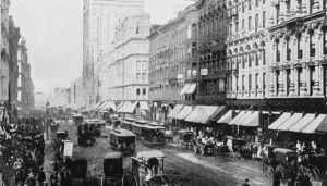 Historical photograph of a street in Chicago in the early 1900s. The street is crowded with horse-drawn carriages, trolleys and early automobiles.