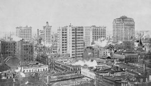 Historical photograph of Chicago with the first high-rises in the background and smaller brick buildings in the foreground.