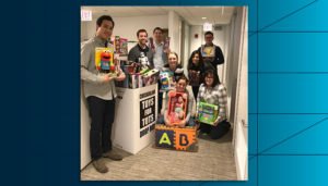 Employees from Draper and Kramer, Incorporated holding toys collected for Toys for Tots in their office space.