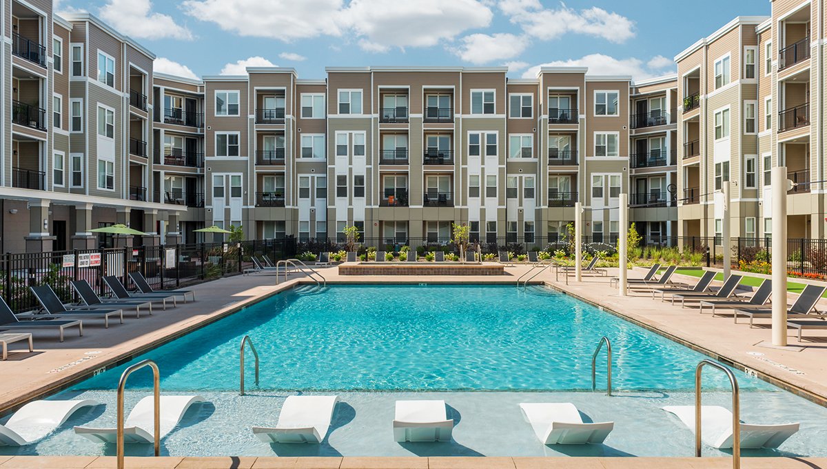 The outdoor pool at EVO Living. The tanning shelf is seen in front with the clear blue salt water of the pool beyond it. EVO Apartments is seen at the far edge.