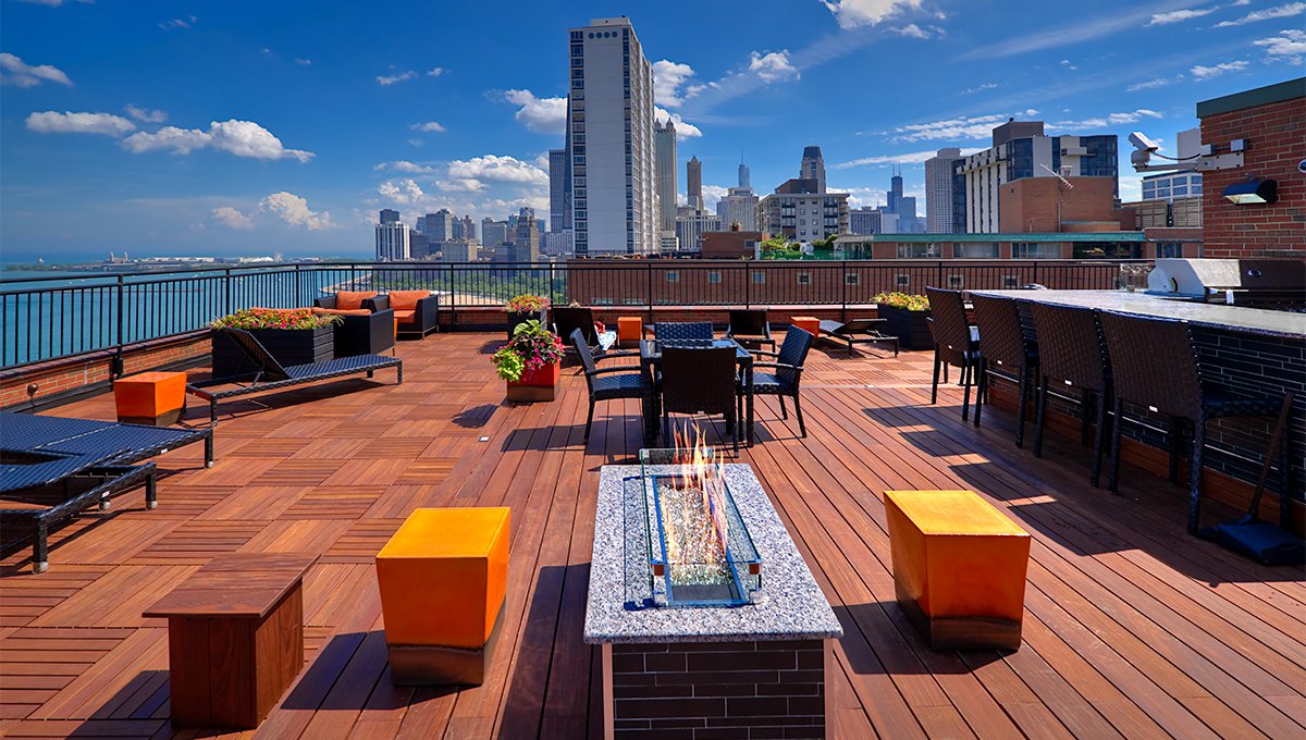 The roof deck of 1350 North Lake Shore apartments on a clear, sunny day. The city of Chicago skyline is the background and an inviting fire pit offers warmth to the seats around it in the foreground.