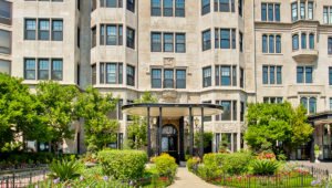 The exterior of 1420 North Lake Shore from the street. A sidewalk leads to the intricate front door and is surrounded by lush greenery and shrubs. The stone building leads up out of the picture and is nestled between the buildings next door on both sides.