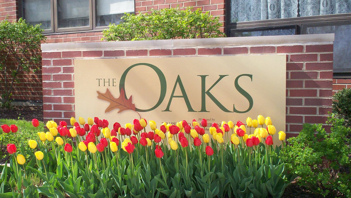 The red brick sign in front of The Oaks with red and yellow tulips in front of it.