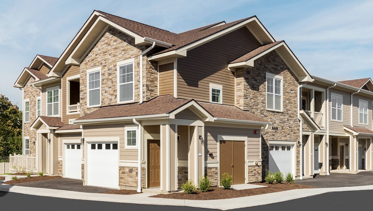 A close, exterior look at EVO Flats at the corner of a building. There are two garage doors to left and one to the right. The main entrance is in the middle. The building is two stories and a mix of brown siding and stone.