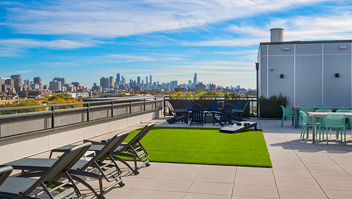 The rooftop deck at Wrigleyville Lofts with the Chicago skyline in the distance. Several lounge chairs line the left with turf and a bags game ahead.