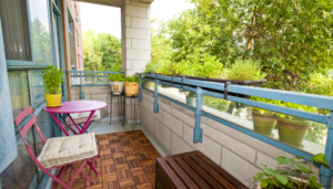 The outdoor deck of an apartment with a small table and chairs, bench and lots of greenery.