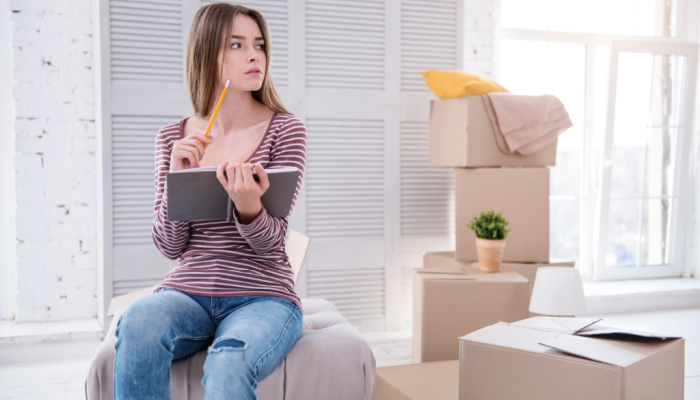 A woman sits on moving boxes while reviewing her move-in checklist.
