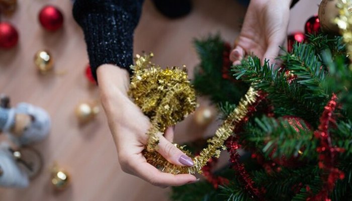 A pair of hands are seen laying garland on a Christmas tree.