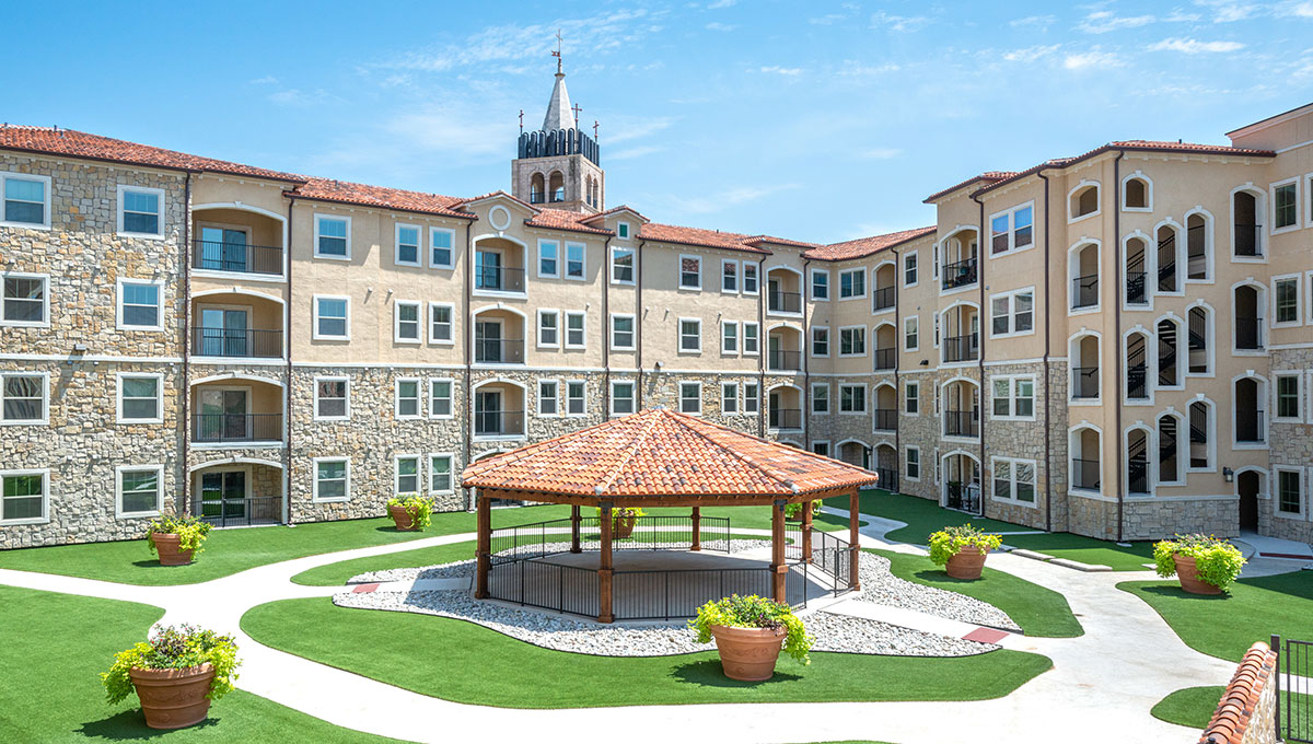 A courtyard at Adriatica Senior Living with the building in the background and a bell tower behind that.