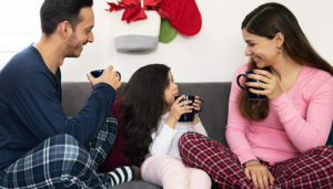 A family enjoys hot chocolate on their couch in pajamas.