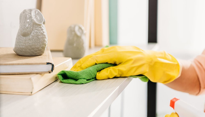 A close-up of a hand wearing a cleaning glove wiping down a shelf.