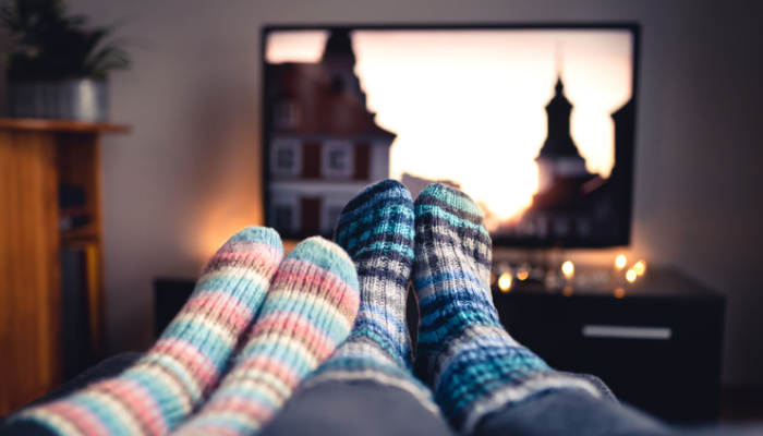 A couple of pairs of feet wearing warm socks kicked up on a coffee table in front of a television screen.