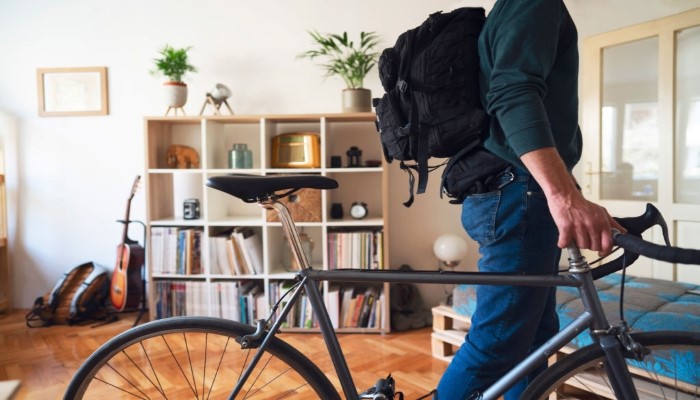 Photo of a young man with his bicycle and backpack, leaving his apartment.