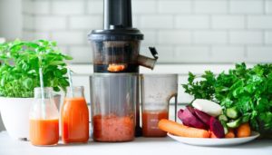 A juicer with various fruits and vegetables around it.