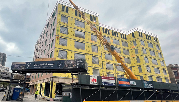 The exterior of the Wrigleyville Lofts development looking up from the street on a cloudy day. The building is surrounded by construction barriers and a crane is parked in front.
