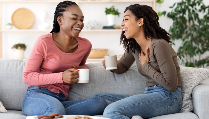 Two women talk on a couch while having coffee.
