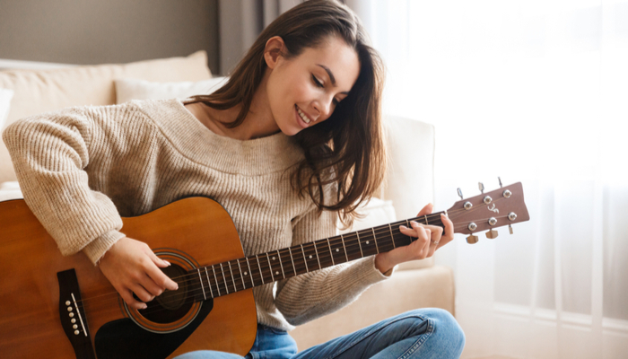 A woman sits on her living room floor and plays the guitar.