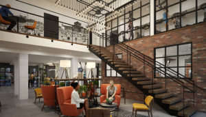 Standing in the lobby, ahead two women sit in large orange chairs talking. There is a staircase to the right that leads up to the fitness center.