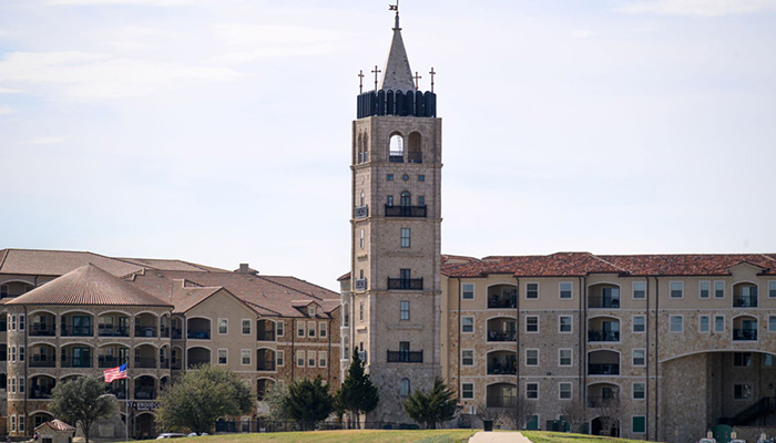 The Adriatica Bell Tower stands tall ahead of the apartment complex, which reaches out to the left and right behind it.