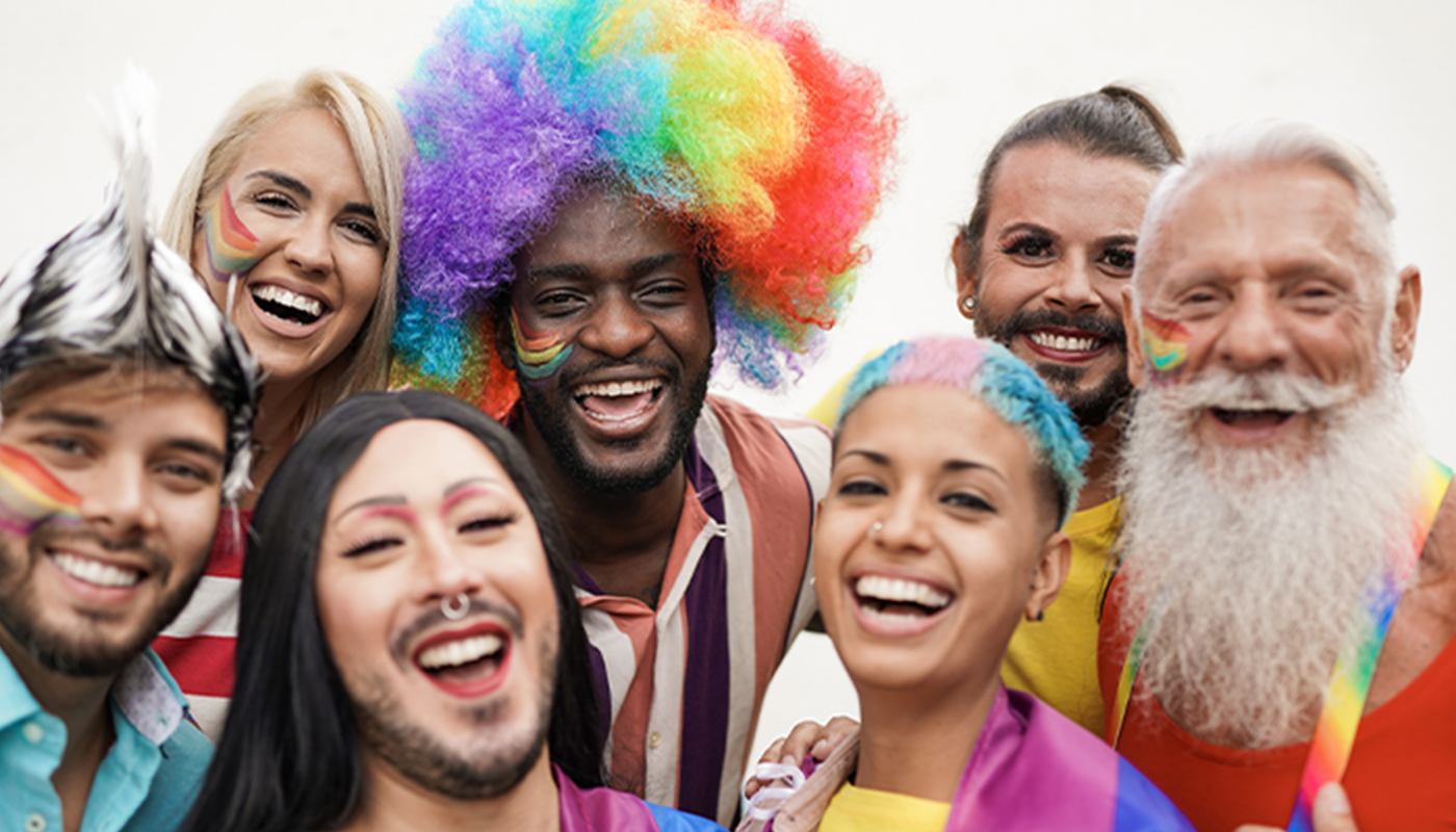 A group people smile at the camera all dressed in bright rainbow colors.