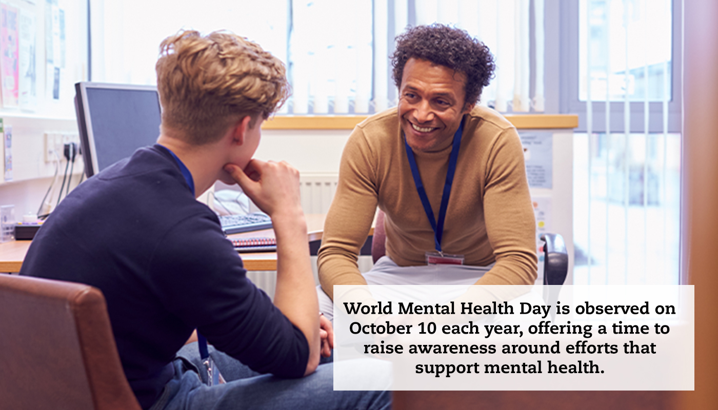 Two men talk to each other across a desk in an office. A quote reads, "World Mental Health Day is observed on October 10 each year, offering a time to raise awareness around efforts that support mental health."