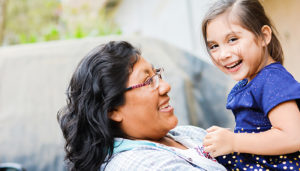 A mother smiles at and holds her young daughter up to the camera.