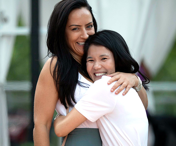 Two woman hug each other and smile happily to the camera.