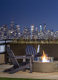 A close look at two chair next to a lit firepit at night on the rooftop deck at Wrigleyville Lofts. The Chicago skyline is seen in the distance.