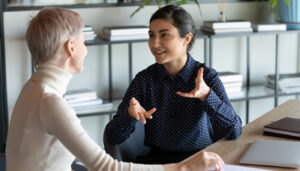 A woman talks with a resident at her desk.
