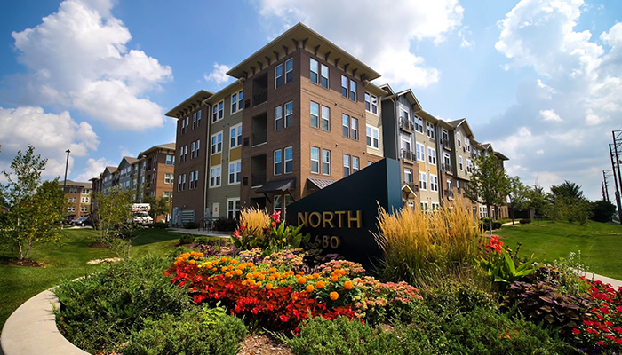 The main entrance sign for North 680 is blue with an angled top and North 680 in gold lettering. Flowers surround the sign. The apartment building is seen behind on a partly cloudy day.