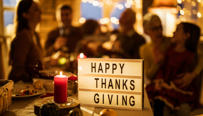 A group of people sitting around a table with a sign that says Happy Thanksgiving.