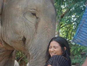 A woman smiles while standing next to an elephant.