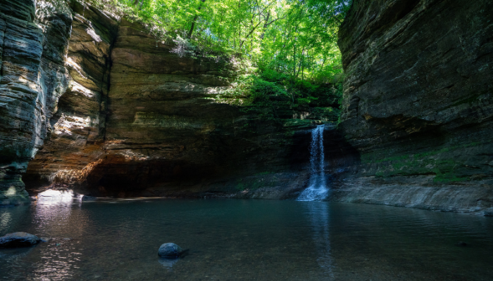 A serene waterfall cascading into a tranquil pool within a forested canyon.