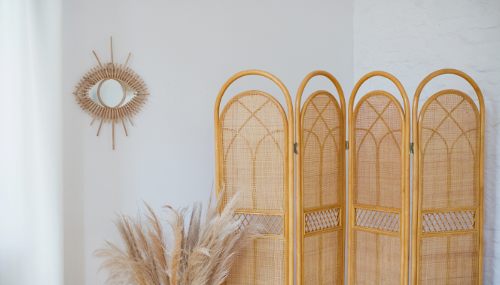Wicker room divider next to a dry pampas grass arrangement in a white room with a small decorative mirror on the wall.