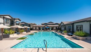 A well-maintained outdoor swimming pool, surrounded by sun loungers and a modern apartment complex under a clear blue sky.