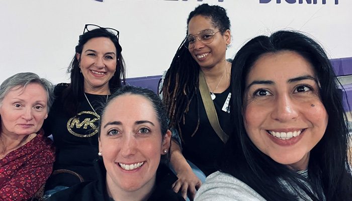 Five women are sitting close together and smiling at the camera.