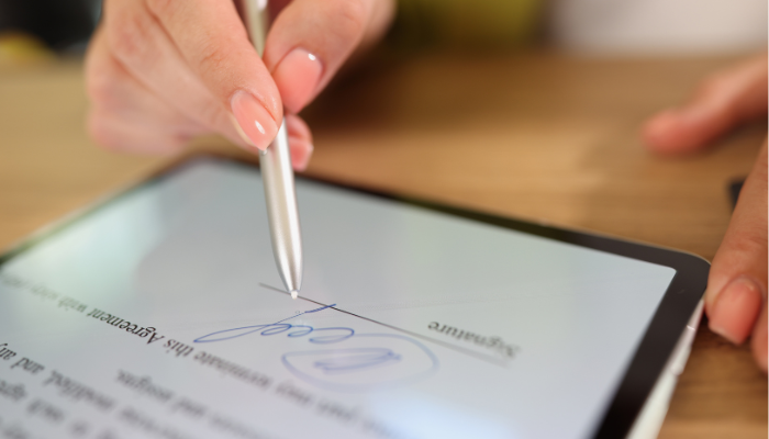 A person signs a digital document on a tablet using a stylus.