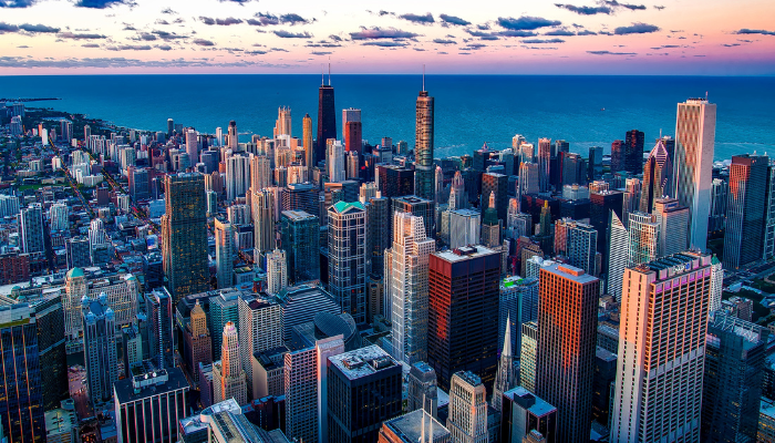 Aerial view of downtown Chicago at sunset, showcasing a skyline filled with high-rise buildings and Lake Michigan in the background.