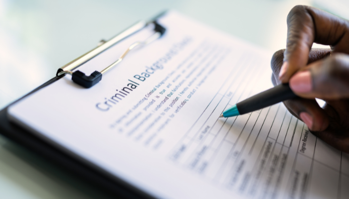 Close-up of a person filling out a criminal background check form on a clipboard, representing the rental application process for first-time renters.