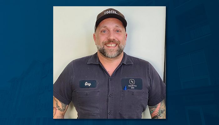 Augustus 'Guy' Coletti, Maintenance Supervisor at North 680, wearing a work uniform with his name badge and smiling warmly while standing against a neutral background.