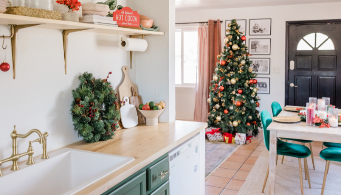 Festively decorated apartment featuring a Christmas tree, a holiday-themed dining table, and a kitchen with green cabinets, a wreath, and seasonal accents.